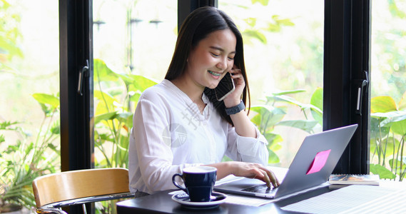 办公室亚洲商业妇女正在使用移动和触摸智能电话进行通信妇女在咖啡店工作时使用笔记本亚洲商业妇女正在使用移动和触碰智能电话进行通信笔图片