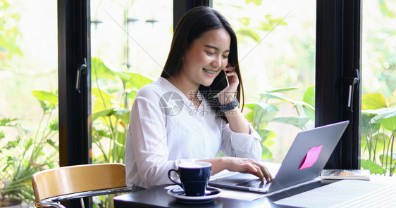 办公室亚洲商业妇女正在使用移动和触摸智能电话进行通信妇女在咖啡店工作时使用笔记本亚洲商业妇女正在使用移动和触碰智能电话进行通信笔图片