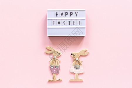 布局桌子季节灯箱文字复活快乐和一对木制兔子在粉红色的纸背景上概念复活节创意自上而下的组合平躺贺卡图片