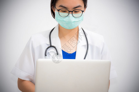 灰色的亚洲年轻女医生佩戴眼镜和面具保护科罗纳的安全看笔记本电脑有听诊器的医生正在用一台电脑来阻止Covid19的流行医生正在用一图片