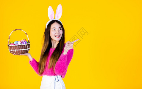 夏天穿着兔子耳朵的亚洲快乐女青年手拿着一个篮子配彩色复活节鸡蛋在黄色空版间工作室背景上孤立无闻亚洲人们图片