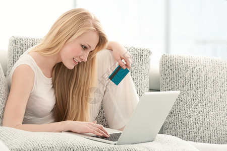 美丽的年轻女在笔记本电脑上用信卡购物坐在客厅的索法Sofa正在做沙发快乐的图片