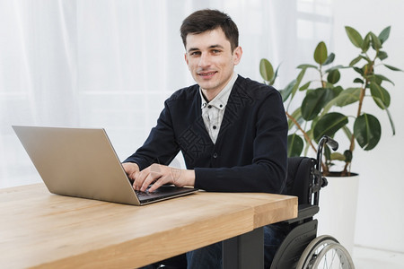 随意的女使用笔记本电脑坐在轮椅上的年轻商人微笑着的肖像工作图片
