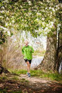 锻炼快乐的一个身着黑绿色衣服的老人在一个温暖的春日里在靠近湖边的森林里跑来去在苹果花下户外图片