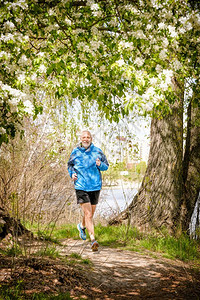 花朵一名身穿黑色和蓝衣服的年长男子在温暖的春日靠近湖边的森林中奔跑在苹果花下一个温暖的春天退休成人背景图片