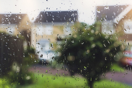 白色的寒冷抽象在雨天窗玻璃上有雨滴树和房子背景都模糊不清在路面下着雨后用水滴纹理看望透的窗户深处图片