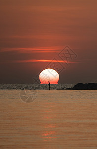 海浪水场景太阳在橙色天空海面上的太阳与岩石上有钓鱼棒的渔夫图片