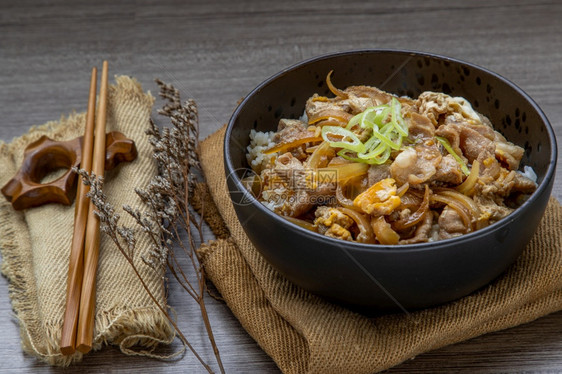 桌子日本猪肉饭碗配鸡蛋和洋葱Donburi在木桌日本菜风格上配有姜咸菜和绿茶木制的筷子图片