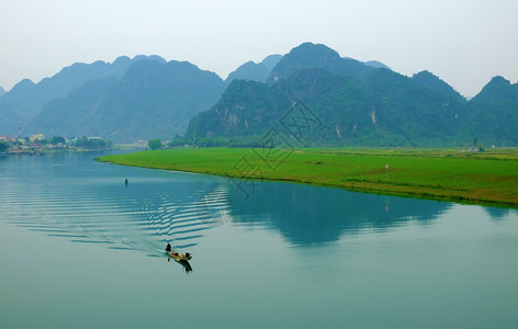 越南的QuangBinh的惊人自然景观白天在越南QuangBinh船在河流上行驶边房屋后面有山脉水旁绿田越南旅行景色美丽仙境人们图片