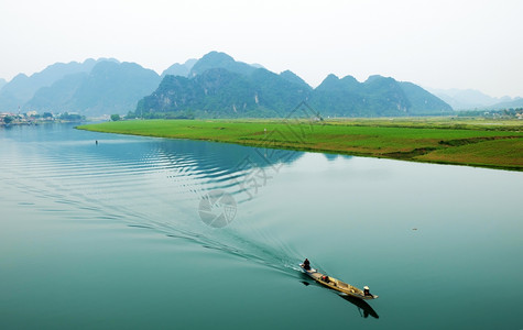 种植园越南QuangBinh的惊人自然景观白天在越南QuangBinh船在河流上行驶边房屋后面有山脉水旁绿田越南旅行景色美丽亚洲图片