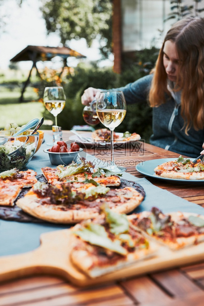夏天家人和朋友在庭花园的夏季野餐户外晚期间用比萨沙拉水果和喝白葡萄酒在家庭花园的夏季野餐户外晚期间喝白葡萄酒午餐假期图片