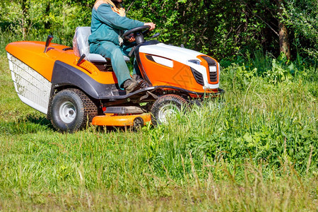 技术在阳光明媚的一天用专业草坪割机在生长过度的草原上种植园丁将高绿色草地与拖拉机割复制成一个园丁和高绿色草地新鲜的杂丛生图片