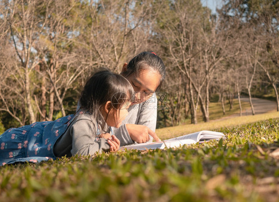 户外亚裔母亲在春花园为女儿念书家人一起度暑假野餐共时间女孩乐趣图片