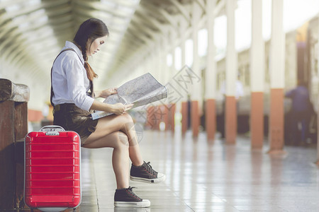 在火车站旅行时亚洲孕妇坐在长椅上看和红色手提箱的皮Holiday旅行概念怀孕父母商业图片