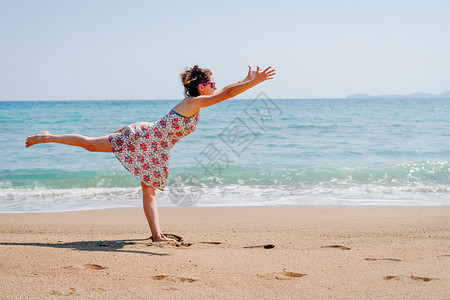 夏天穿着衣服的年轻女子在海边滩做瑜伽在阳光明媚的白天裙子冥想年轻的图片