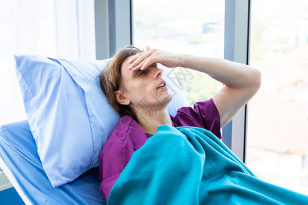 一名男患者头痛并因焦虑而发烧躺在房间医院背景的床上面对焦虑的脸疾病治疗医的图片