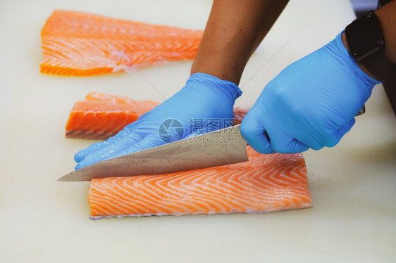 切片沙门鱼主厨切开新鲜生鲑鱼片餐桌上的剪板有一把尖利刀手紧餐厅生鱼片图片