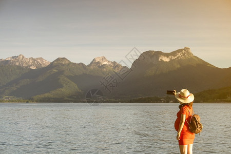 幽思裙子在大山前的码头上湖边自拍穿着跟踪帽子和红礼服的女孩在大山前面的码头上服用图片