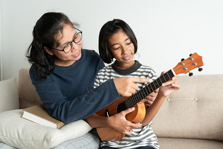 亚裔母亲教她女儿在自己家客厅沙发上坐时教她女儿玩乐游戏长椅音活的图片