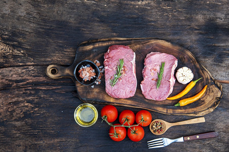 美食在厨房的木板餐桌背景上有迷迭香盐大蒜番茄黑辣椒橄榄油肉牛排和制品的木板上肉肋骨小牛图片