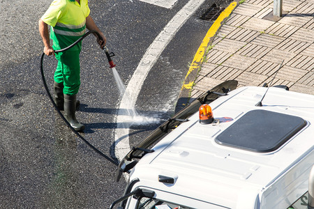 肮脏的工人用高压水清洗道路和街人行的清洁工洗涤公司高清图片