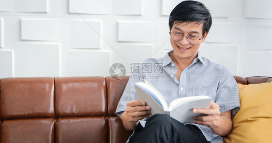 房间亚裔老人在家中客厅里读沙发的书亚洲老年男子的肖像正在放松和家阅读杂志时幸福快乐退休卧室图片