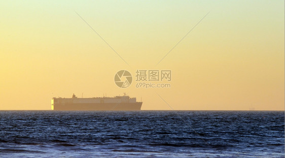明亮的大部分日落时地平线上的大型集装箱货船轮廓图片
