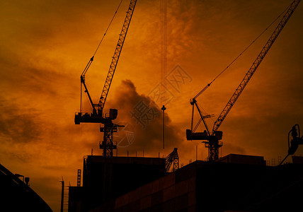 活动戏剧在高楼建筑上造起重机在黄昏日落时用橙色天空和云状的巨型橙色天空建造高楼起重机建造商业筑或城市背景共区城市的图片