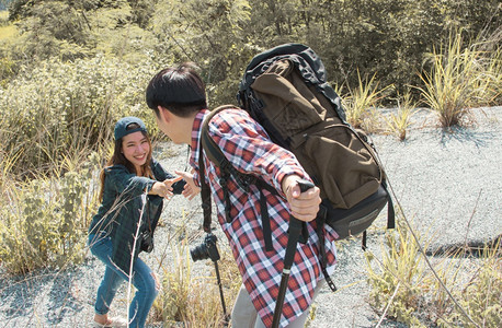 背包爬山顶峰一个背着包的亚洲男子帮助女人通过握拉手爬山旅行和夏天概念TriverandSummerConception运动朋友背景