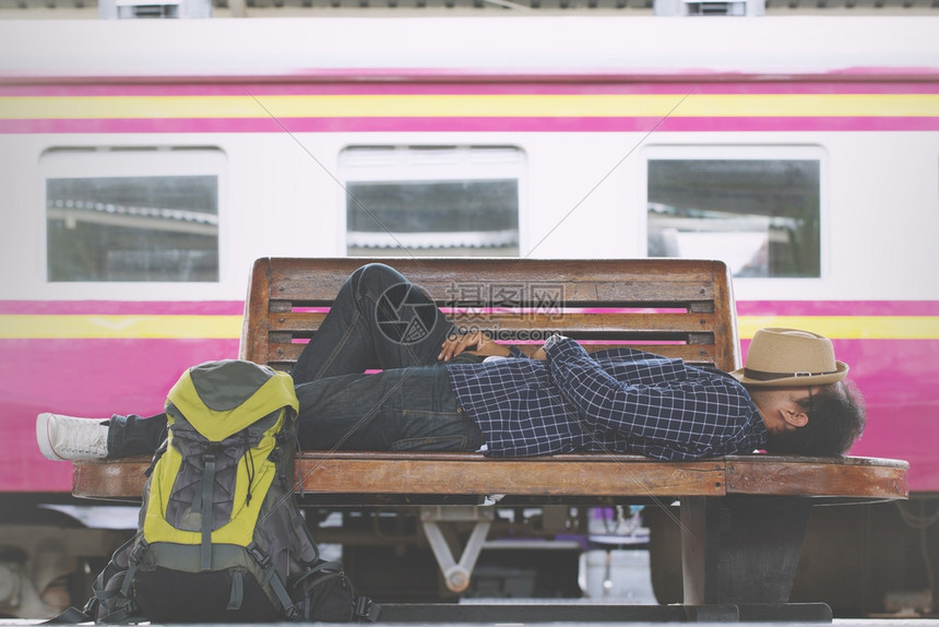 年轻男子旅行者睡觉在火车站的轮椅上等候火车去旅行度假离开天户外图片