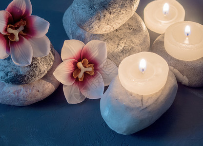 蓝色背光紧贴的斯帕和在石上花竖着燃烧的白蜡烛闪光丝帕以及站在石上和花着的烧白蜡烛植物治疗水图片