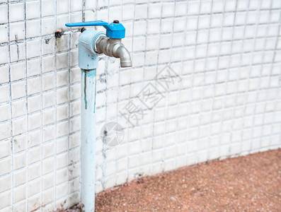 蓝色水龙头在城市房屋的瓷墙旁边有肮脏的管子白色道金属图片
