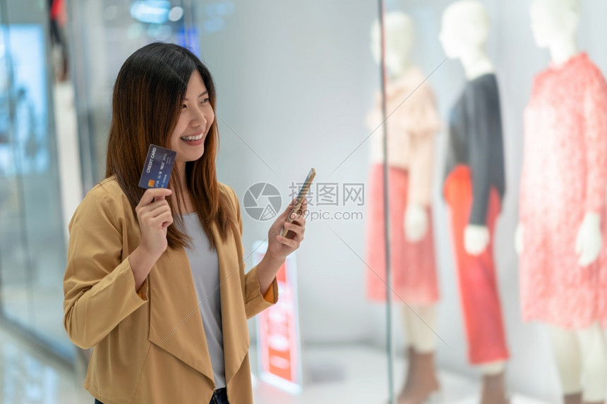 互联网亚洲妇女利用信卡和移动电话在百货商店通过服装背景技术钱财包和网上支付概念信用卡模型在线购物亚洲妇女使用信卡和移动电话在服装图片