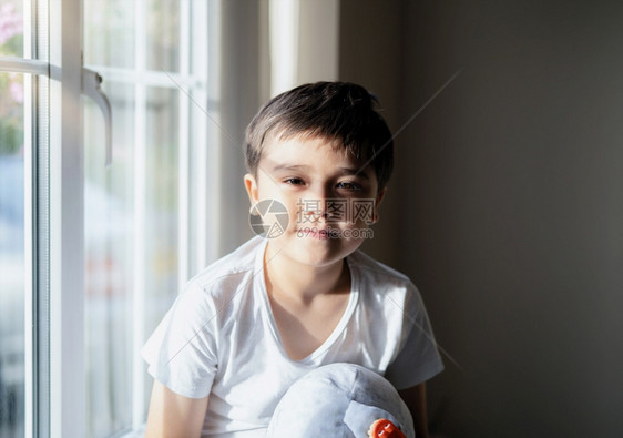 男生秋天坐在窗户旁边的快乐男孩晚上秋夜光照在窗边高关灯可爱的小男孩带着微笑的脸看相机周末独自在家玩具的童子男孩英俊图片