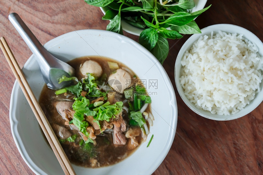 杯子一顿饭亚洲风格鲜牛肉面条汤和木制桌上的蒸米饭白碗里带猪球的牛肉面条蒸水稻和新鲜鱼美食图片