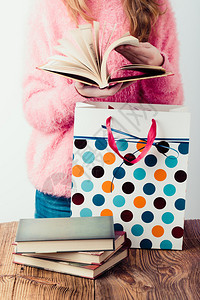 学习请享用在书店翻页的年轻女孩把书写成纸袋几本书放在一个穿粉红色毛衣和蓝牛仔裤垂直照片的木制桌青少年女孩身上棕色的图片