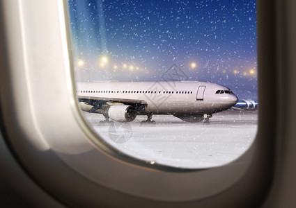在非飞行天气时通过飞机窗口查看场和白色飞在非行天气时到达下雪的除冰图片