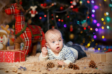 小男孩躺在房间里肚子上带着圣诞装饰品坐在房间里快乐的前夕散景图片