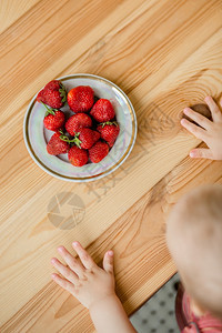 吃白色的乐趣乡村背景中带草莓的孩子手一盘草莓夏季健康饮食的概念从上面看公寓乡村背景中带草莓的孩子手一盘草莓图片