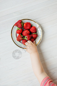 诱惑乡村背景中带草莓的孩子手一盘草莓夏季健康饮食的概念从上面看公寓乡村背景中带草莓的孩子手一盘草莓吃水果图片