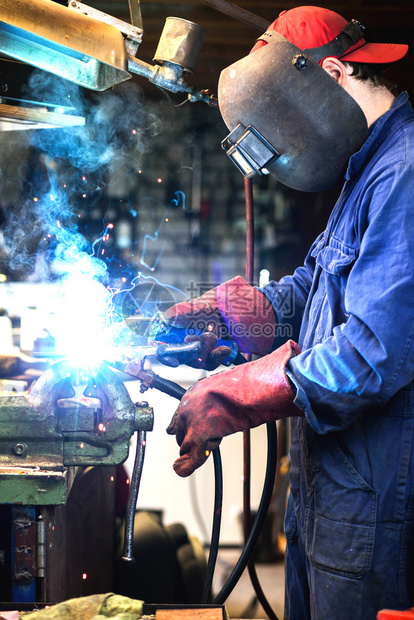 焊工正在用防护面罩焊接车库中的金属零件工业钢焊作机正在用防护面罩焊接车库中的金属零件工业钢焊机匠行氩气图片