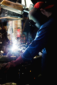 头盔闪光焊工正在用防护面罩焊接车库中的金属零件工业钢焊作机正在用防护面罩焊接车库中的金属零件工业钢焊机厂图片