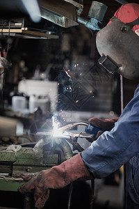 火焊工正在用防护面罩焊接车库中的金属零件工业钢焊作机正在用防护面罩焊接车库中的金属零件工业钢焊机面具建造图片