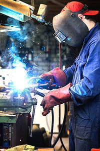 劳动工厂焊正在用防护面罩焊接车库中的金属零件工业钢焊作机正在用防护面罩焊接车库中的金属零件工业钢焊机技术的图片