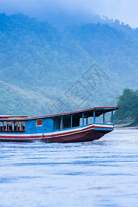 蓝色的清晨在湄公河上的传统木船背景为北老挝LuangPrabang的蓝山和雾森林景观图片