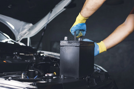 手套发动机自由械手正在拉起一辆旧车的电池以更换图片