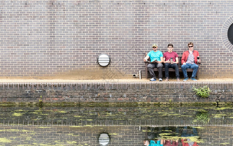 水三个男朋友喝咖啡在运河滨附近享受坐着愉快闲暇学生图片