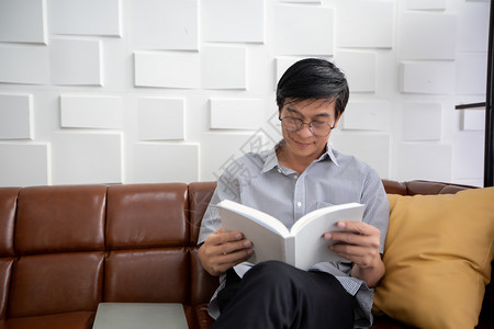 亚裔老人在家中客厅的沙发上读书亚洲老年男子的肖像正在放松和幸福与阅读杂志内部的抓住公寓图片