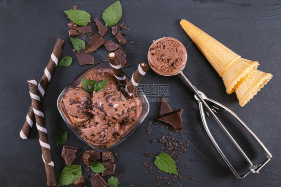 把巧克力冰淇淋放在玻璃碗里配有面包棒甜瓜和巧克力在黑板上集中关注碗配有勺子巧克力冰淇淋冷冻凉爽的茶点图片