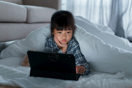 说谎亚洲小女孩晚上在卧室的毯子下使用平板数字片码教育房间图片